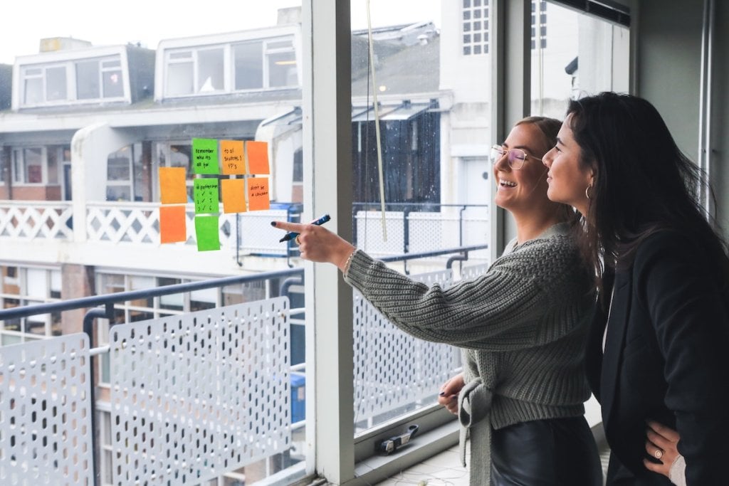 Two women brainstorming using Post-Its on a window