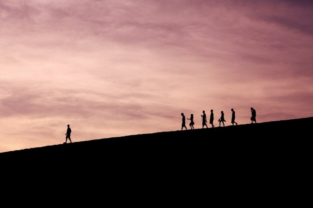 Silhouettes of people walking down a hill. One is in front